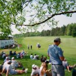 Masters tickets - Spectators watch golfers on a sunny day at a tournament.